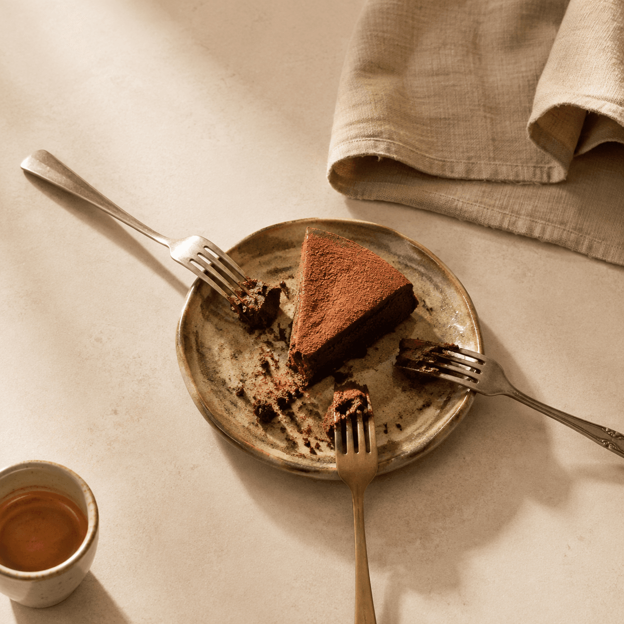 Uma fatia de bolo de chocolate compartilhada por três garfos, ao lado de um café